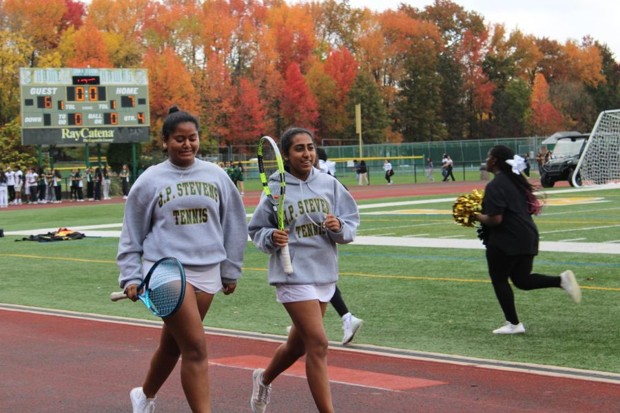 The girls varsity tennis captains senior Jiya Saxena and senior Vidhi Malik run across the track at the Fall Athletics Recognition Assembly.